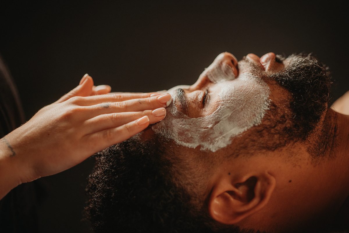 Soin du visage douceur : application du masque blanc sur le visage d’un homme allongé