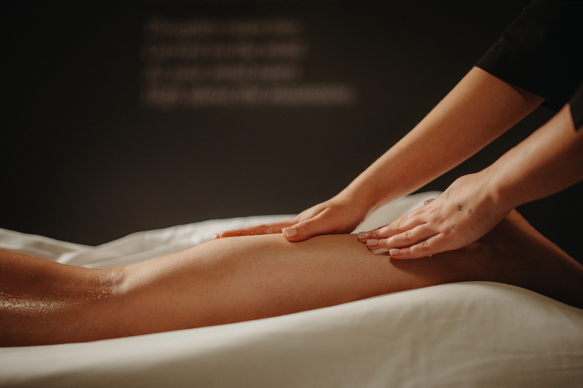 Massage des jambes, mains frottant une huile sur la jambe allongée